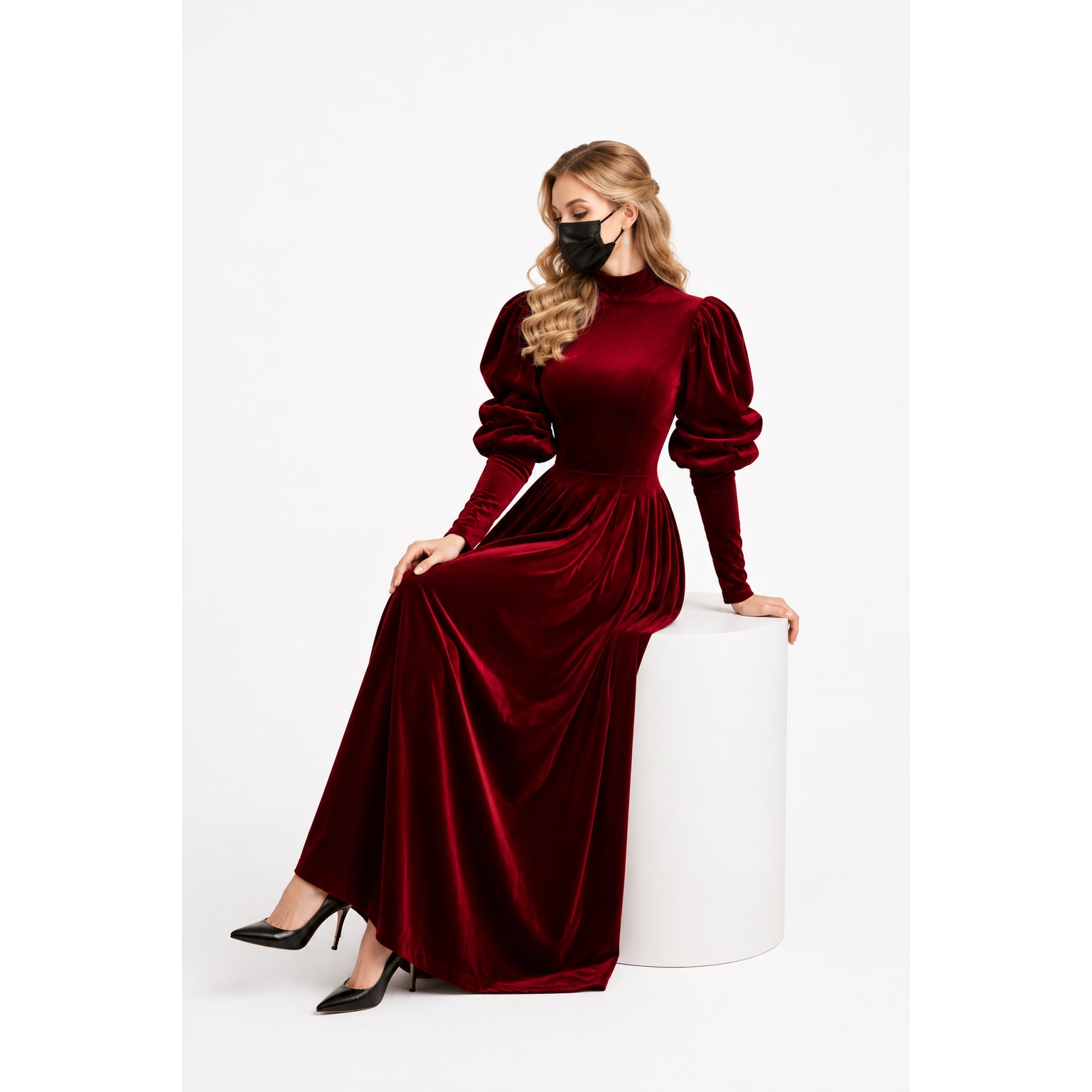 Woman in elegant burgundy velvet sissy maid dress with puff sleeves, seated on white pedestal.