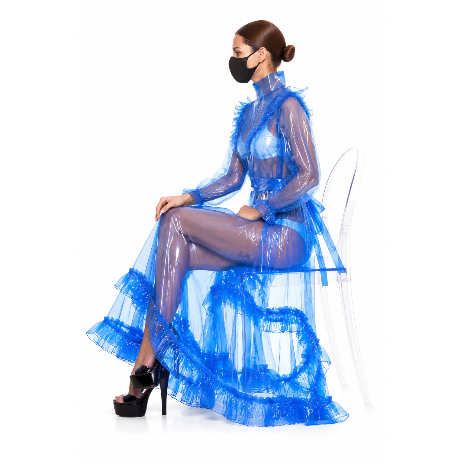 Blue sissy maid dress with ruffles, sheer overlay, and high heels, seated on clear chair