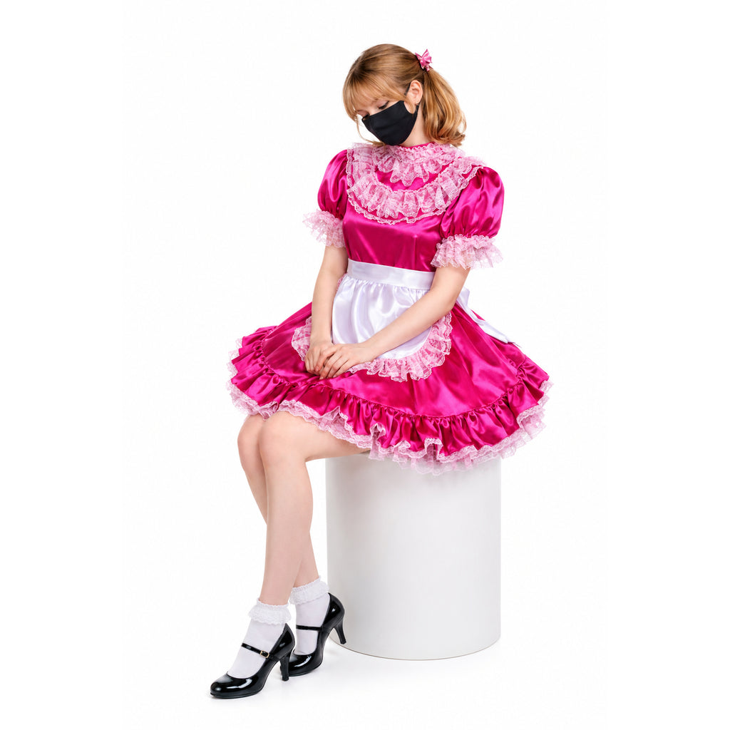 Pink sissy maid dress with lace ruffles, white apron, and black heels, worn by seated model on white pedestal