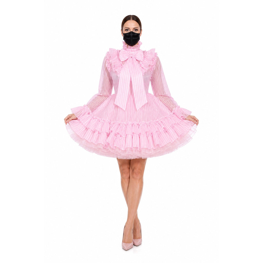 Pink sissy maid dress with ruffles, bow, and sheer sleeves, styled with heels and face mask