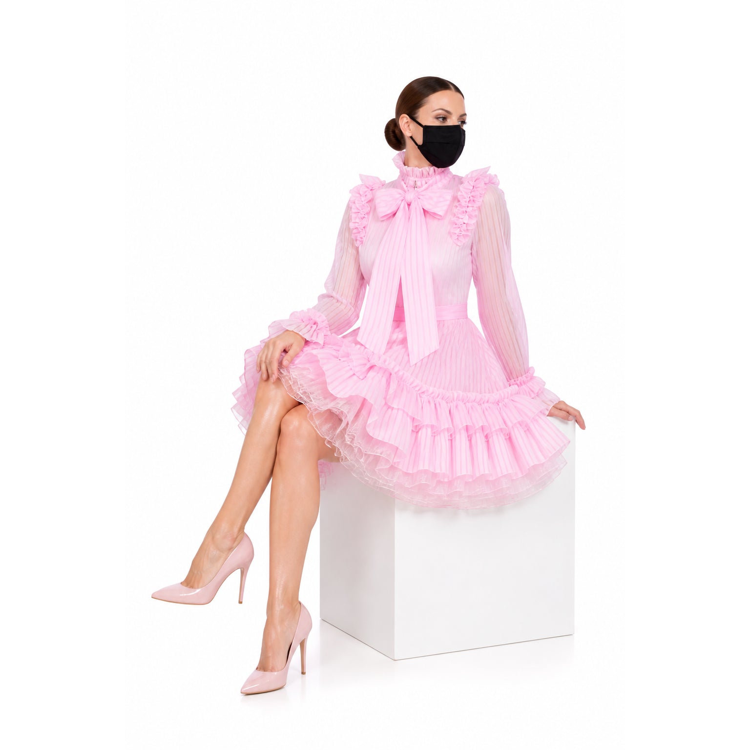 Pink sissy maid dress with ruffles, bow, and sheer sleeves, paired with heels, worn by seated model.