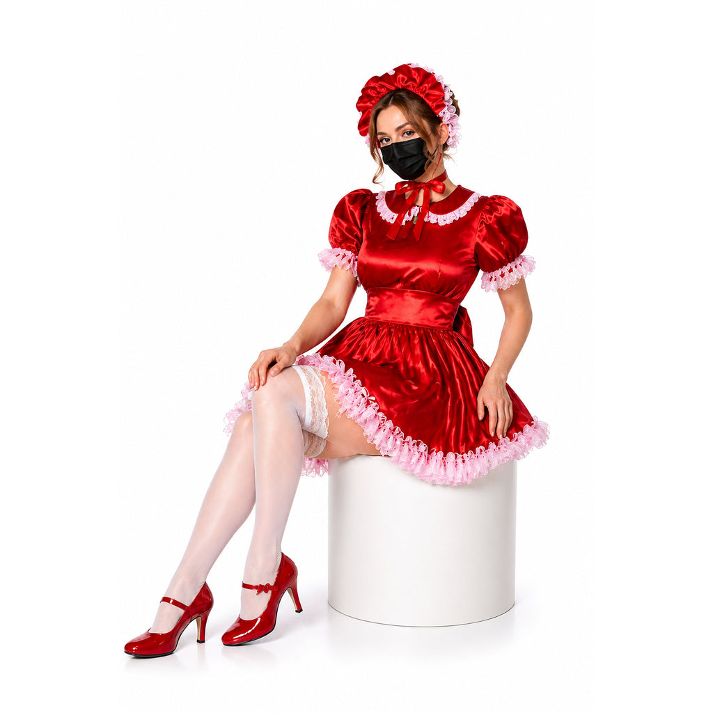 Red sissy maid dress with pink lace trim, matching bonnet, and heels, worn by seated model on white pedestal.