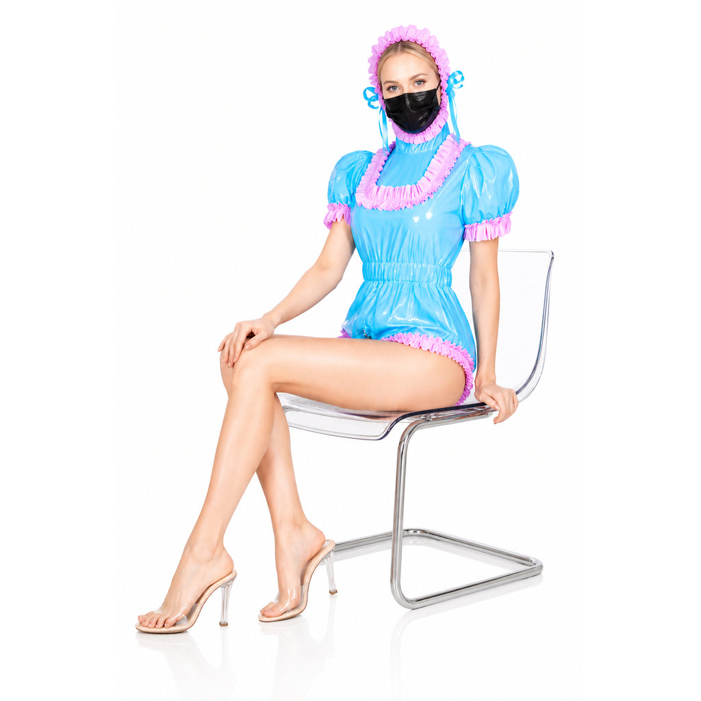 Blue PVC sissy maid dress with pink ruffles, bonnet, and mask, styled with clear heels on modern chair