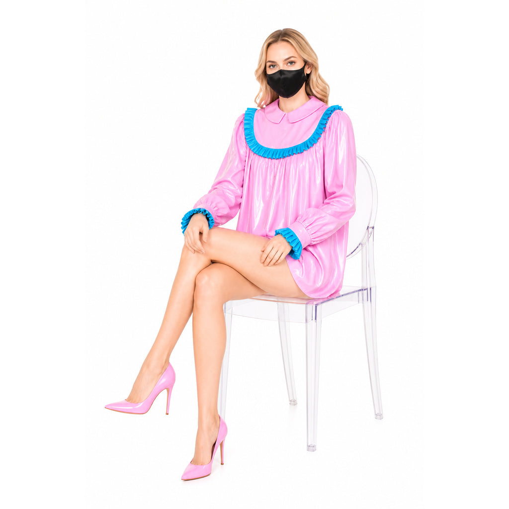 Pink PVC sissy maid dress with blue ruffles, paired with matching heels, worn by seated model.